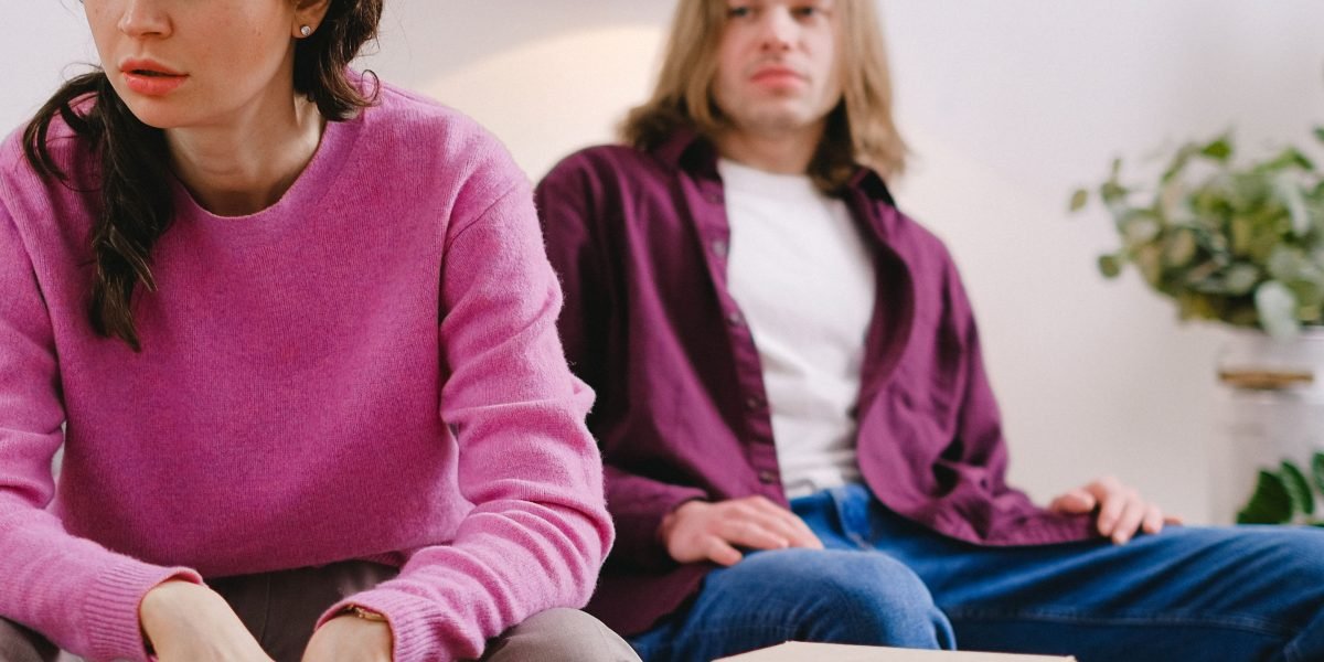 A couple sitting on a couch, appearing distant or withdrawn from each other, reflecting relationship anxiety.
