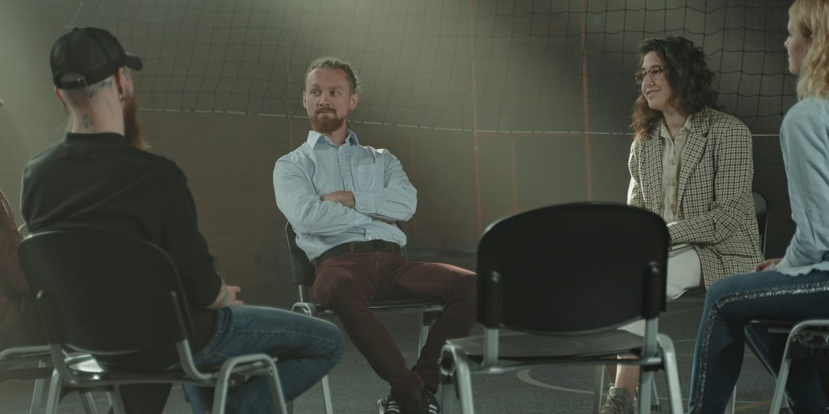A diverse group of individuals in a meeting, engaging in conversation and offering mutual support.